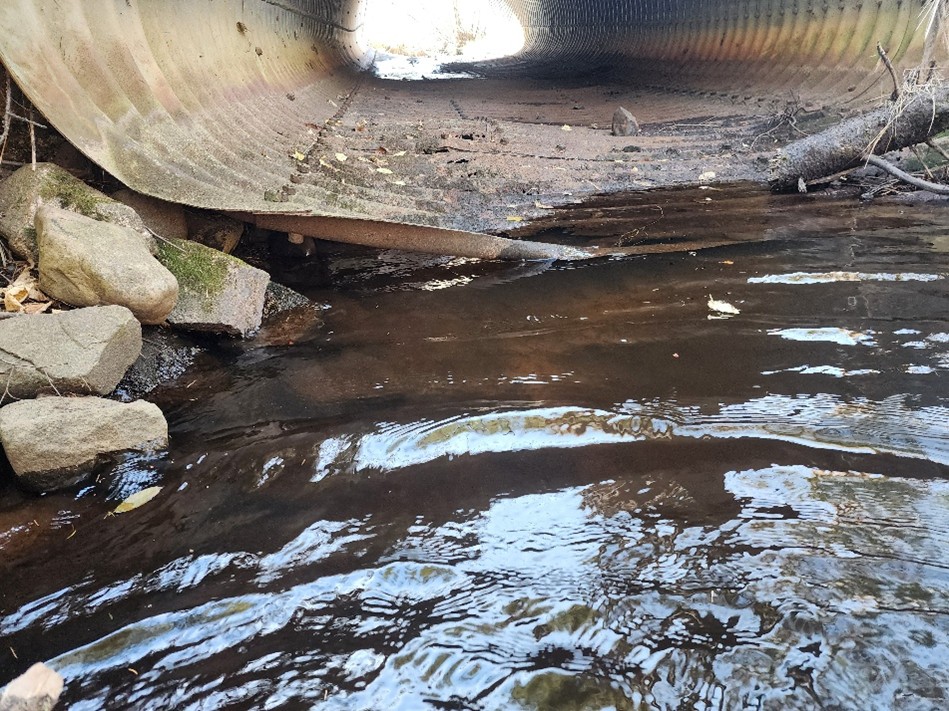 Deteriorating culvert interior at Happy Creek showing corrosion and water flowing through holes in the floor