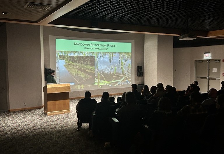 A presenter delivering a lightning talk on the Manoomin Restoration Project at the 2026 LSC Symposium