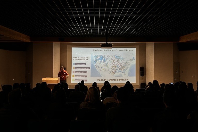 A presenter showing a Freshwater Resilient and Connected Network map during a lightning talk at the 2026 LSC Symposium